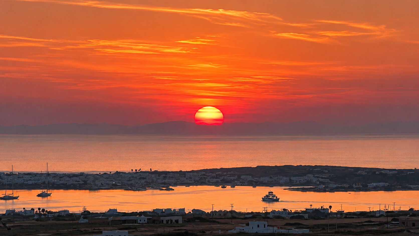 Vista d'un capvespre a la costa amb vaixells, una petita vila i un cel serè.