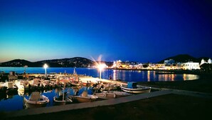 Un puerto deportivo al anochecer con barcos amarrados, un muelle que se adentra en aguas tranquilas y un paisaje urbano al fondo.