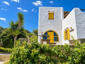 A white building with a yellow door and window shutters, surrounded by greenery and stone walls. - Hilltop Home Sea Views & Terrace Dining near Aliki (ageria)