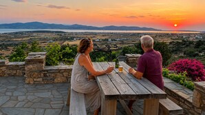 Dos personas sentadas en una mesa de madera con vistas a un paisaje al atardecer.