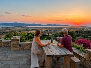 Deux personnes sont assises à une table en bois, devant laquelle s’étend un paysage illuminé par le soleil couchant.