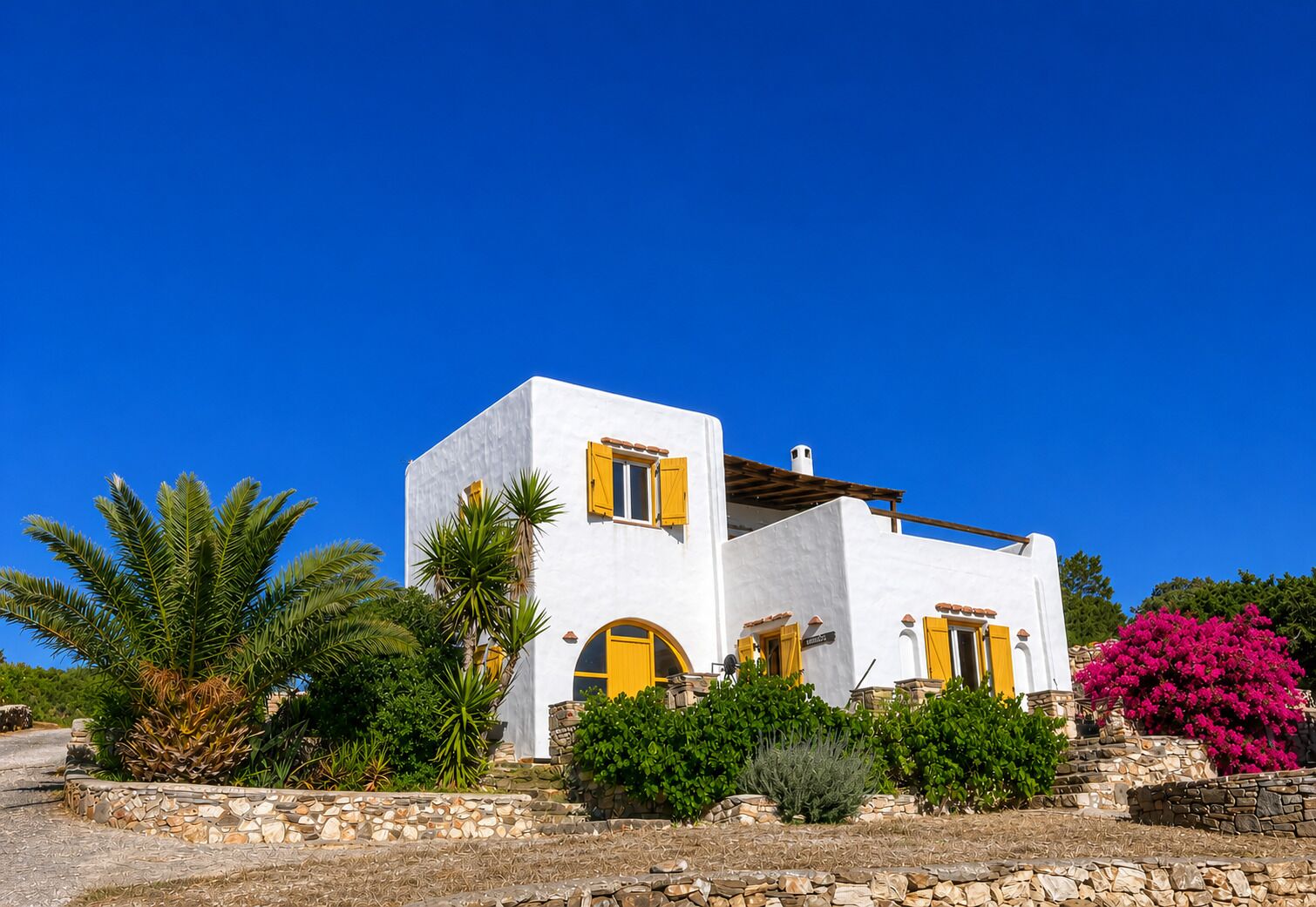 A white building with yellow doors and windows, surrounded by greenery and a clear blue sky.