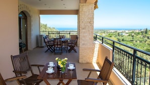 A balcony with a table set for two, a stone pillar, and a view of the landscape.