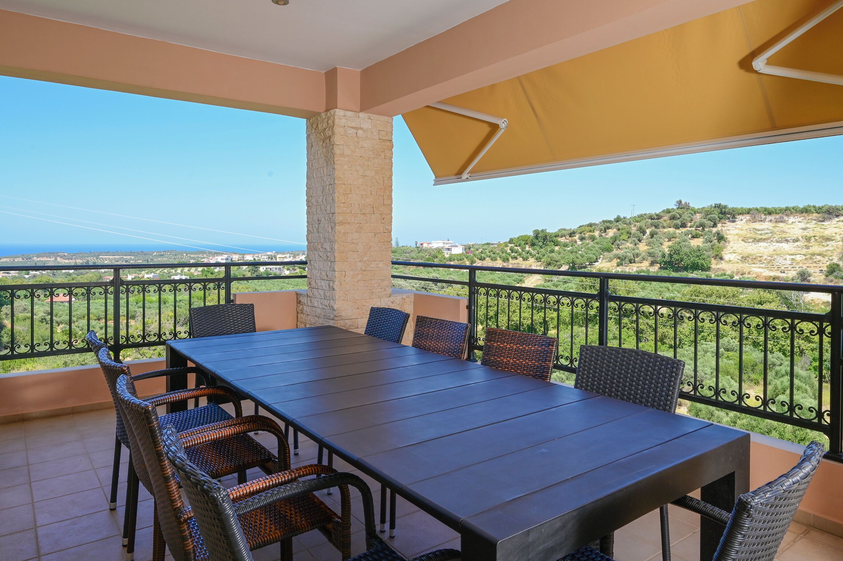 Un balcon avec une table et des chaises, un pilier en pierre et une vue sur un paysage vallonné.