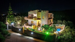 A multi-story house with a swimming pool, surrounded by a stone wall and illuminated by street lights.