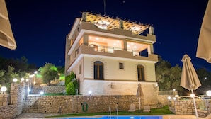 A multi-story building with a swimming pool, stone walls, and outdoor lighting.