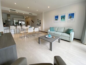Una sala de estar moderna con un sofá gris, una mesa de centro y un comedor con sillas blancas y una mesa de vidrio.