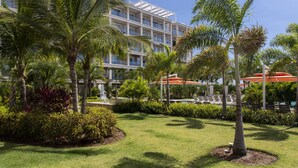 Un hôtel au design moderne, avec une structure à plusieurs étages dotée de balcons et d’un jardin bien entretenu, agrémenté de palmiers et d’arbustes.