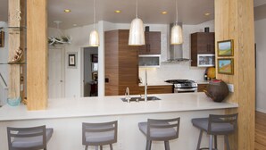 Une cuisine moderne dotée d’un îlot central, de tabourets de bar, de luminaires suspendus, de meubles de rangement en bois et d’une cuisinière en acier inoxydable.