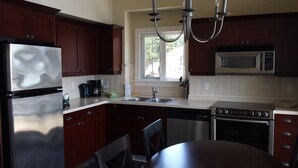 Una cocina moderna con armarios de madera oscura, electrodomésticos de acero inoxidable, un lavamanos doble y un comedor con mesa y sillas.