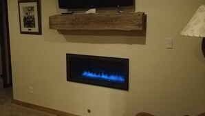 Een woonkamer met een wandtelevisie, een open haard en een houten plank.