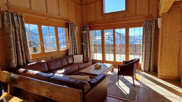 A wooden interior with a sofa, coffee table, and a TV. Large windows offer a mountain view. - Magnificent views, maximum sunshine, dream skiing, absolute peace and quiet, walks  (veysonnaz)
