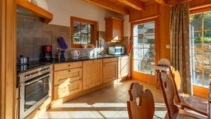 A kitchen with wooden cabinets, a stove, and a dining area with a wooden chair. - Magnificent views, maximum sunshine, dream skiing, absolute peace and quiet, walks  (veysonnaz)