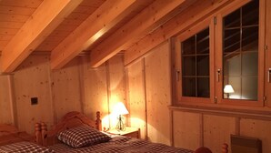 A wooden cabin bedroom with a bed, a nightstand, a lamp, and a window. - Magnificent views, maximum sunshine, dream skiing, absolute peace and quiet, walks  (veysonnaz)