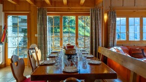 A wooden dining room with a table set for four, large windows, and a stone wall visible through the glass doors. - Magnificent views, maximum sunshine, dream skiing, absolute peace and quiet, walks  (veysonnaz)
