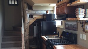 Une cuisine avec un plan de travail en bois, une cuisinière, un évier et un réfrigérateur. Un escalier mène à un autre niveau.