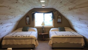 Une chambre mansardée accueillante, avec deux lits, une fenêtre avec des rideaux, une petite table et une chaise.