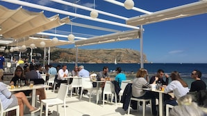 An outdoor dining area with white tables and chairs, a clear view of the sea, and a rocky hillside in the background. - Idyllic & luxury huge 7 bed / bath villa, heated pool & Jacuzzi Wifi (Xàbia)