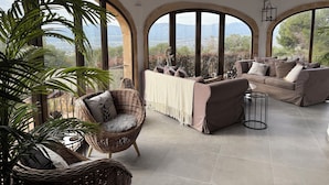A spacious living area with a large window offering a scenic view, a wicker chair, a sofa, and a small table. - Idyllic & luxury huge 7 bed / bath villa, heated pool & Jacuzzi Wifi (Xàbia)