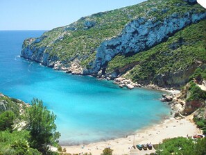 Eine Küstenlandschaft mit Strand, felsigen Klippen und klarem, blauem Wasser.