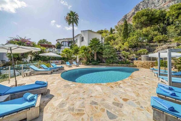 A swimming pool with lounge chairs and umbrellas, surrounded by stone flooring and greenery. - Idyllic & luxury huge 7 bed / bath villa, heated pool & Jacuzzi Wifi (Xàbia)