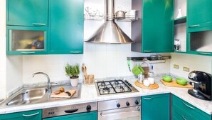 A modern kitchen with teal cabinets, stainless steel appliances, and a central range hood. - Amazing seaview apartment Nervi - Genova (Genova)