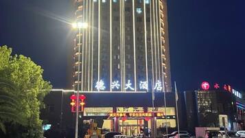 A tall building with illuminated signage, a street with vehicles, and a traffic light.