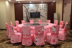 A conference room with a round table, pink chairs with Hello Kitty designs, a flat-screen TV, and a decorative wall. - Dexing Hotel (Dexing)
