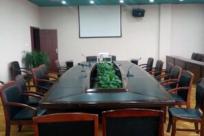 Un salón de conferencias con una larga mesa, sillas, una pantalla de proyector y una planta.