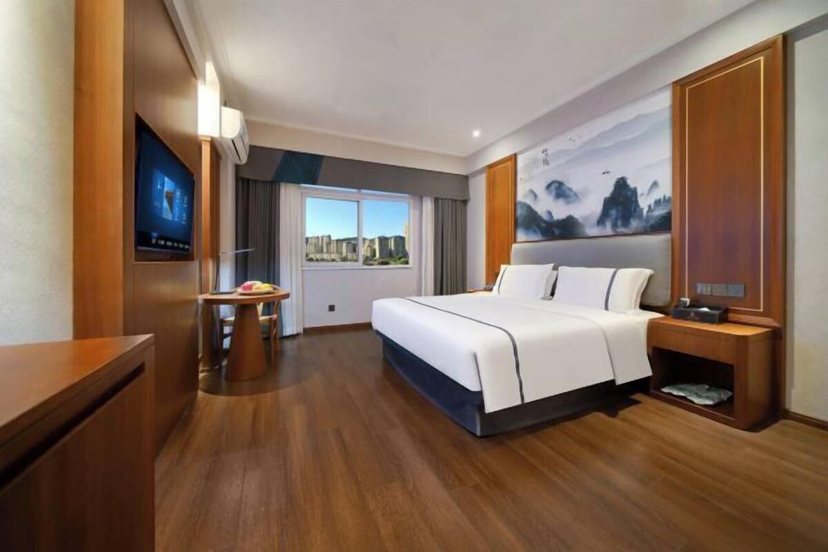A hotel room with a bed, a desk, a TV, and a city view.