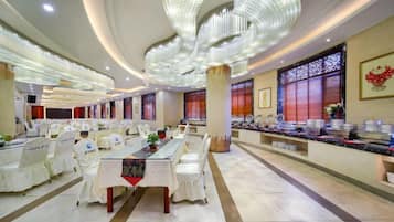 A hotel dining area with round tables, chairs, and a buffet setup.