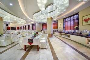 A hotel dining area with round tables, chairs, and a buffet setup. - Dexing Hotel (Dexing)