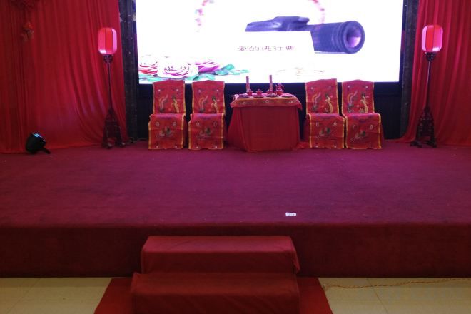 A stage with a red carpet, a table with a red tablecloth, and several chairs with red and gold patterns.