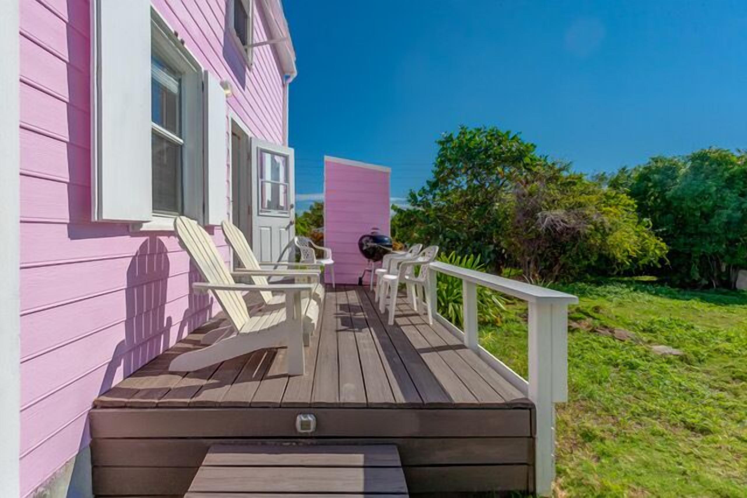 Uma casa cor-de-rosa com um deck de madeira, grades brancas e área de estar externa.