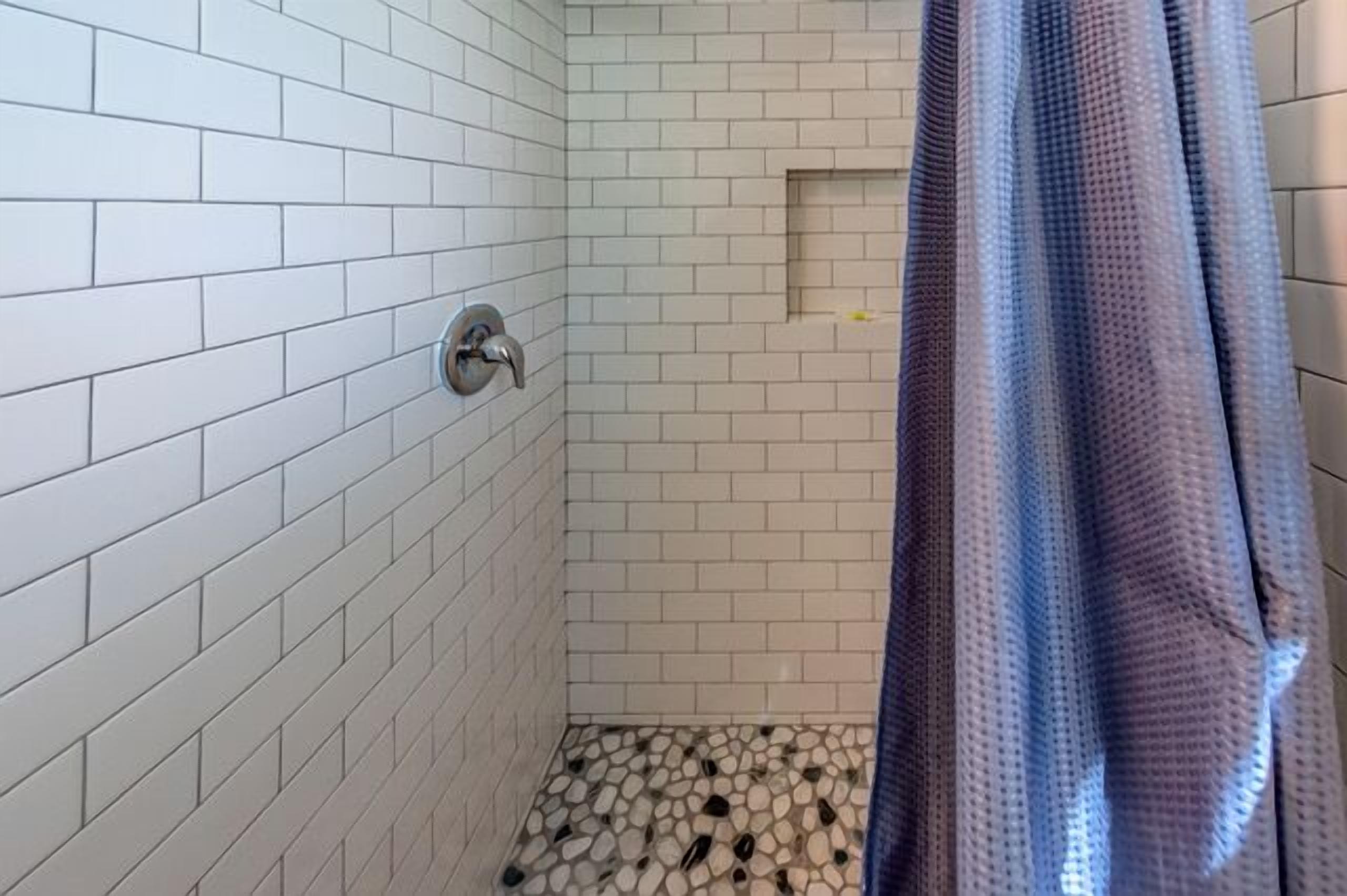 A small shower area with white tiled walls and a pebble-patterned floor.