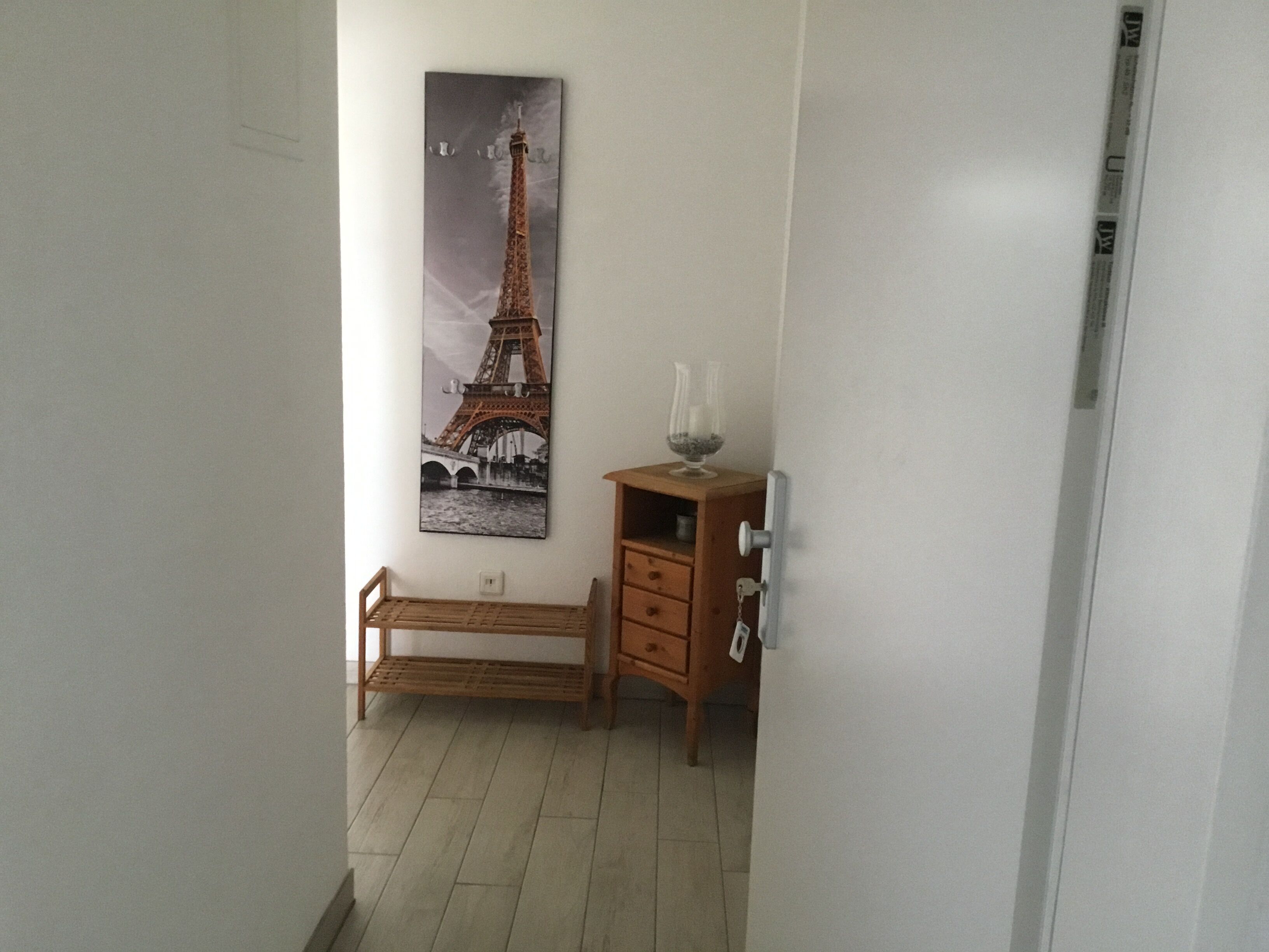 A hallway with a wooden bench, a small wooden cabinet with a glass vase, and a framed picture of the Eiffel Tower on the wall.