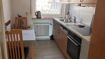 Cozinha compacta com armários de madeira, forno embutido e janela que traz luz natural.