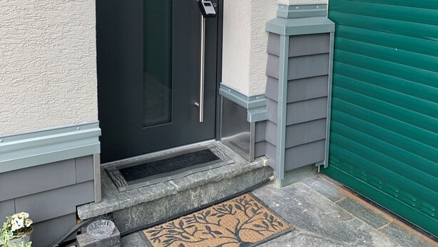 A black door with a vertical handle, a green garage door, and a stone doormat. - 3-room vacation apartment, 64 square meters, with private parking in Ötlingen 79576, Weil am Rhein, near Basel/A5; accommodates up to 6 people (Weil am Rhein)