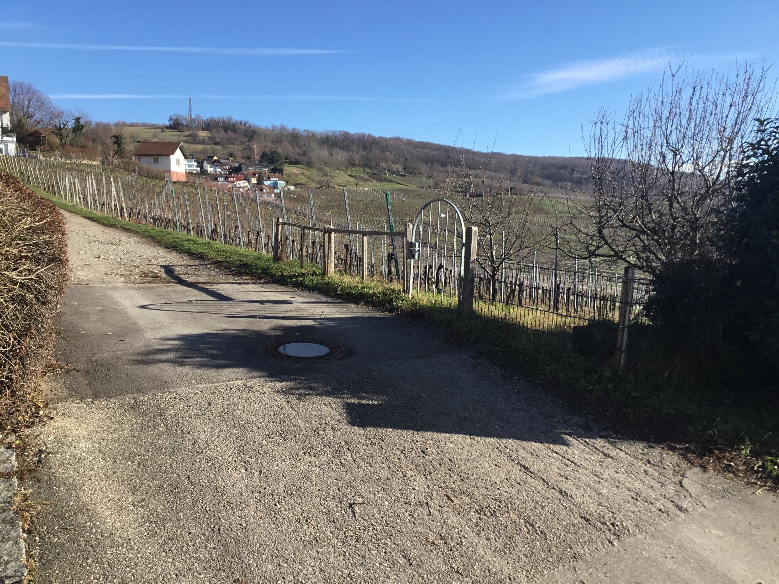 A rural road leading to a gated area with a metal gate and a manhole cover.