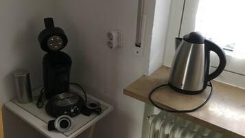 Cozinha compacta com cafeteira, chaleira e uma pequena mesa com um alto-falante e outros dispositivos eletrônicos.