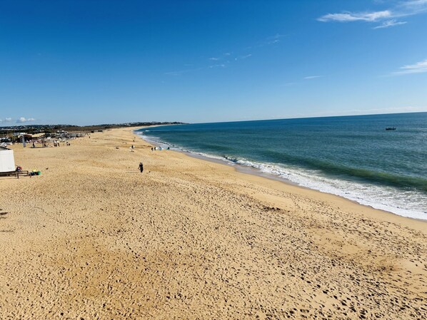 Une vaste plage de sable fin parsemĂ©e dâempreintes, un ciel bleu azur et une mer calme.