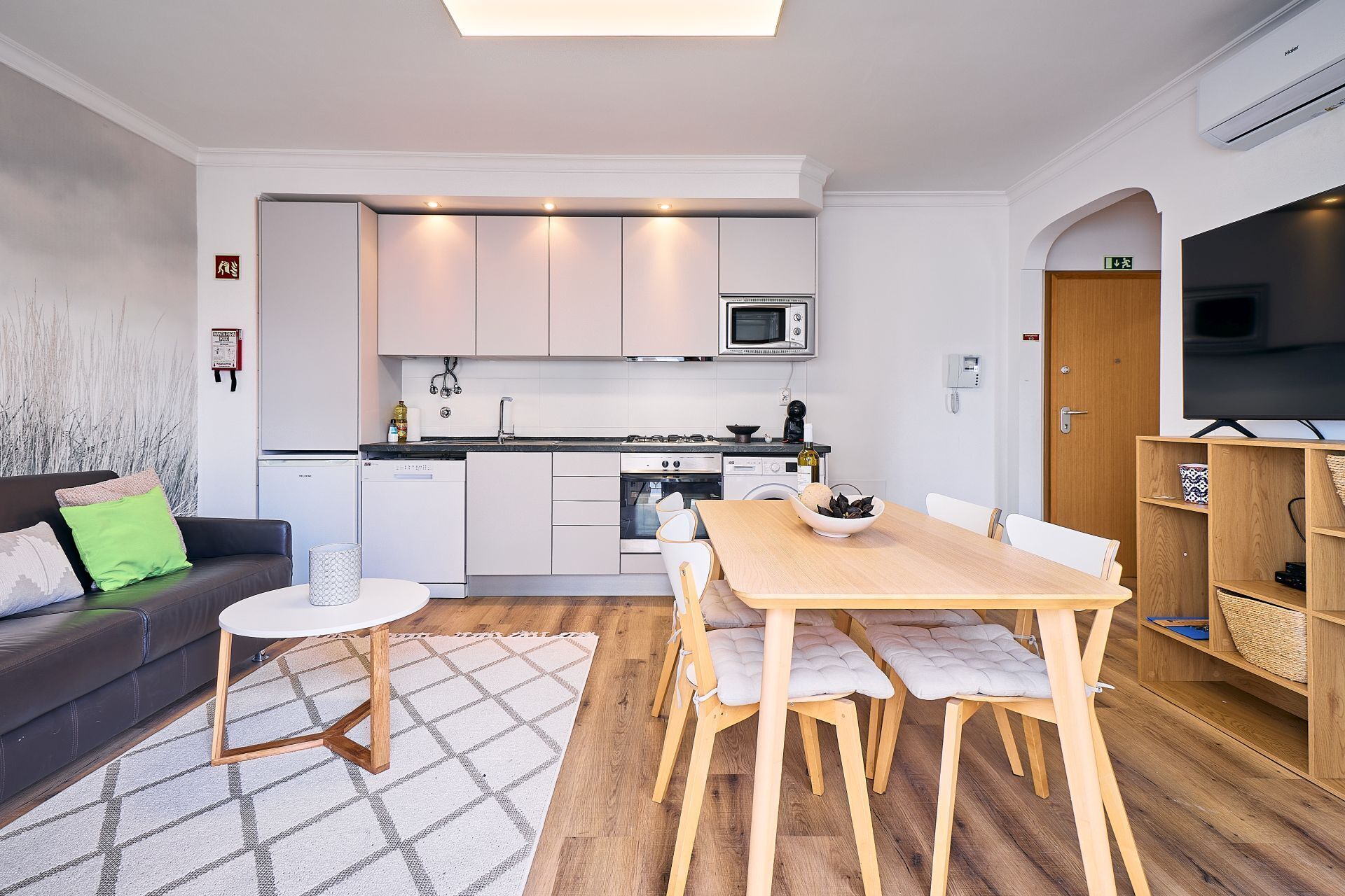 Een moderne keuken met witte kasten, een magnetron, fornuis en een eethoek met tafel en stoelen.