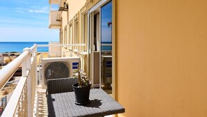 Een balkon met een rieten tafeltje, een bloempot en een airconditioner.