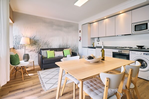 A modern kitchen with a microwave, stove, and washing machine. There's a dining area with a table and chairs.