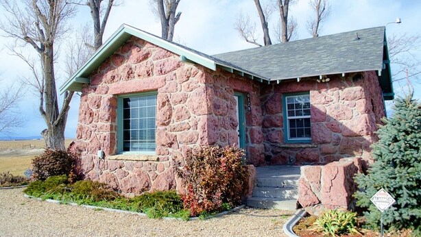 A stone house with a gabled roof, a front porch, and a small front yard with shrubs and a tree. - Red Rock House on the edge of Marsing. 2 Bedrooms 1 Bath (Marsing)