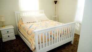 A white four-poster bed with a colorful quilt, a bedside table with a lamp, and a chair against the wall. - Red Rock House on the edge of Marsing. 2 Bedrooms 1 Bath (Marsing)