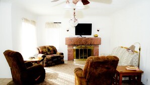 A living room with a fireplace, two armchairs, a sofa, a television, and a lamp. - Red Rock House on the edge of Marsing. 2 Bedrooms 1 Bath (Marsing)