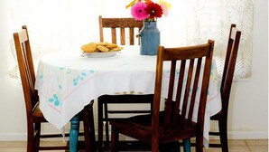 A dining table with a white tablecloth, surrounded by wooden chairs with turquoise legs, and a vase with flowers on the table. - Red Rock House on the edge of Marsing. 2 Bedrooms 1 Bath (Marsing)