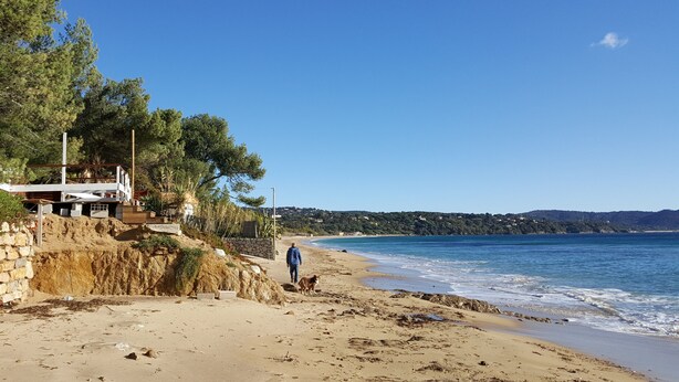 A beach with a wooden structure, a stone wall, and a person walking a dog. - Quiet holiday villa with pool and stunning sea views for up to 10 people (Cavalaire-Sur-Mer)
