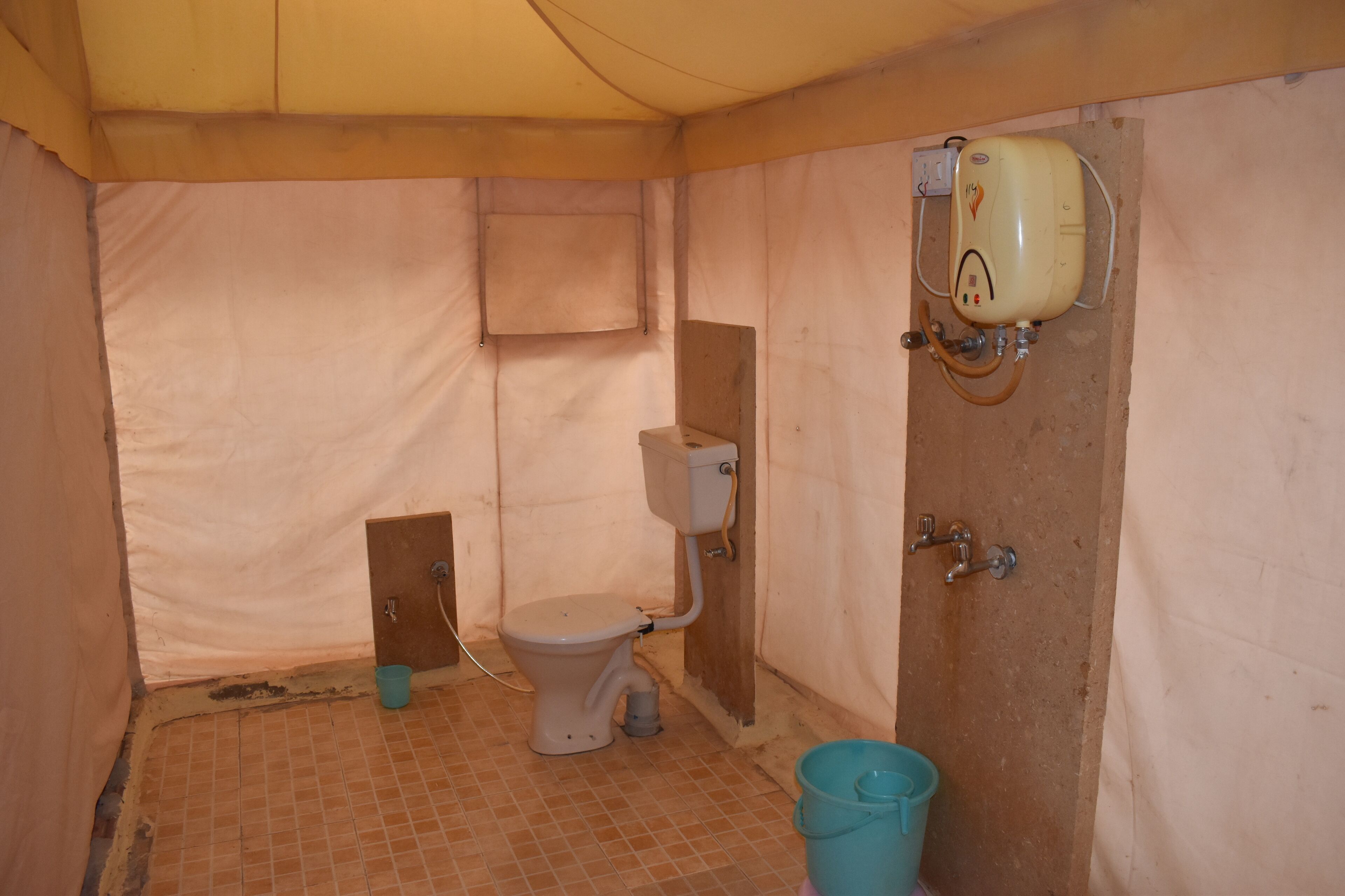 Un baño pequeño y cerrado con un inodoro, calentador de agua y un balde.